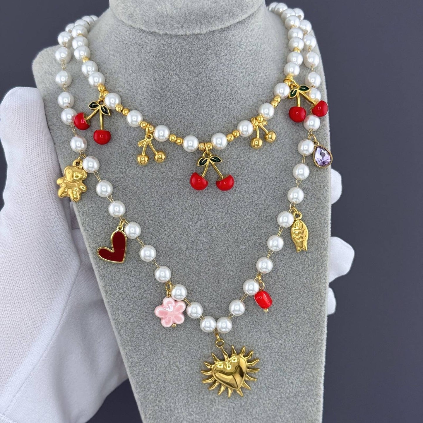 Pearl necklace with colorful charms on a gray stand against a dark background