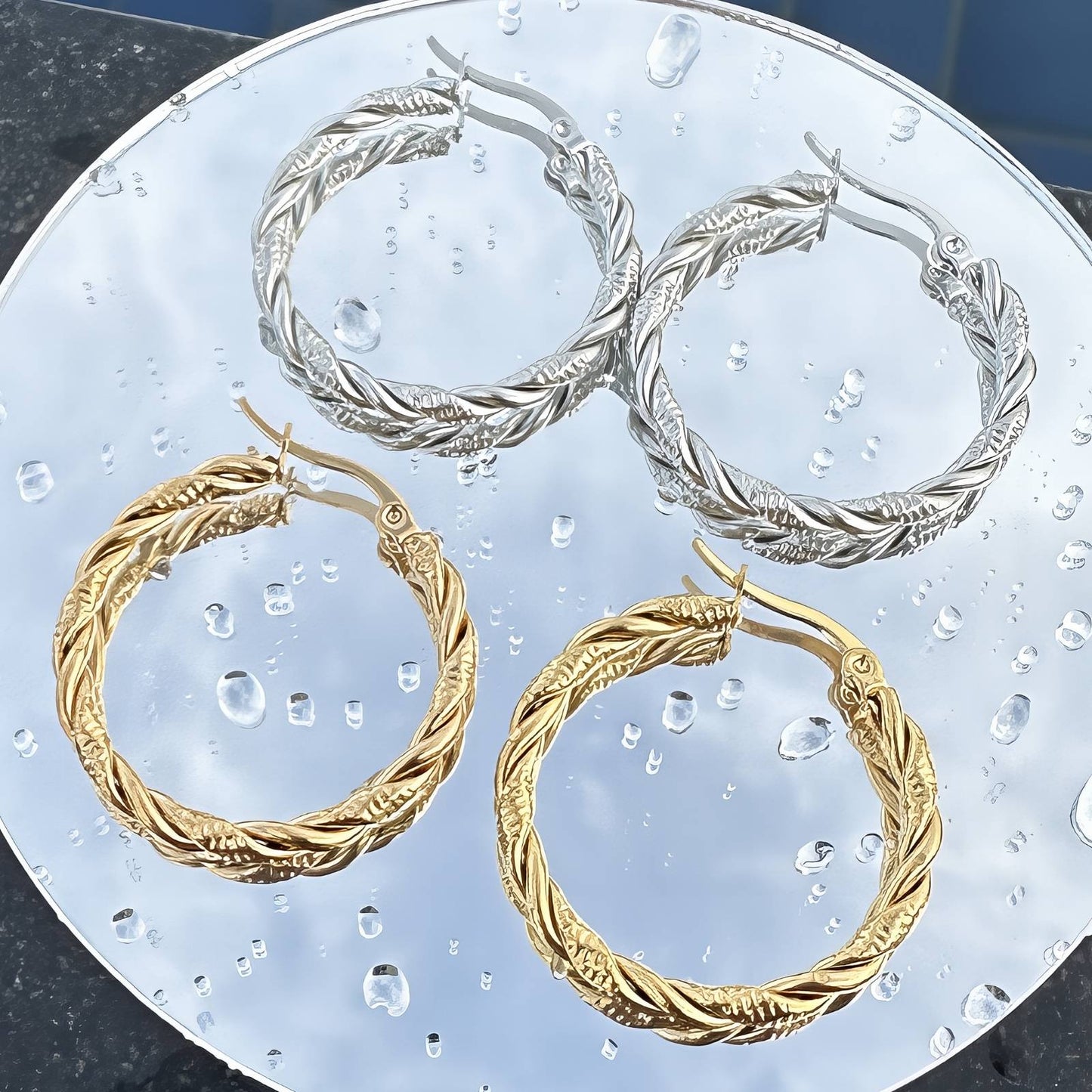 Two pairs of hoop earrings, one gold and one silver, on a textured surface.