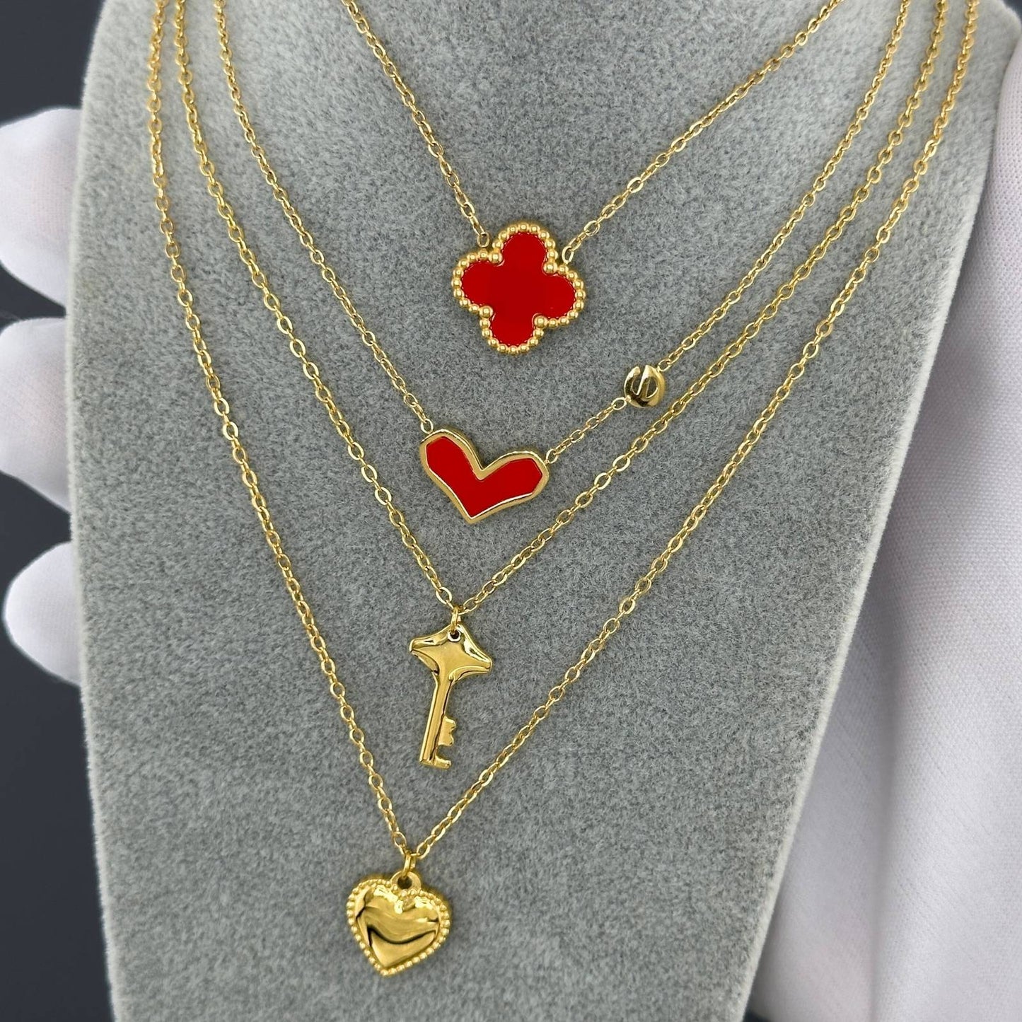 Gold necklaces with red heart and key pendants on a gray stand.