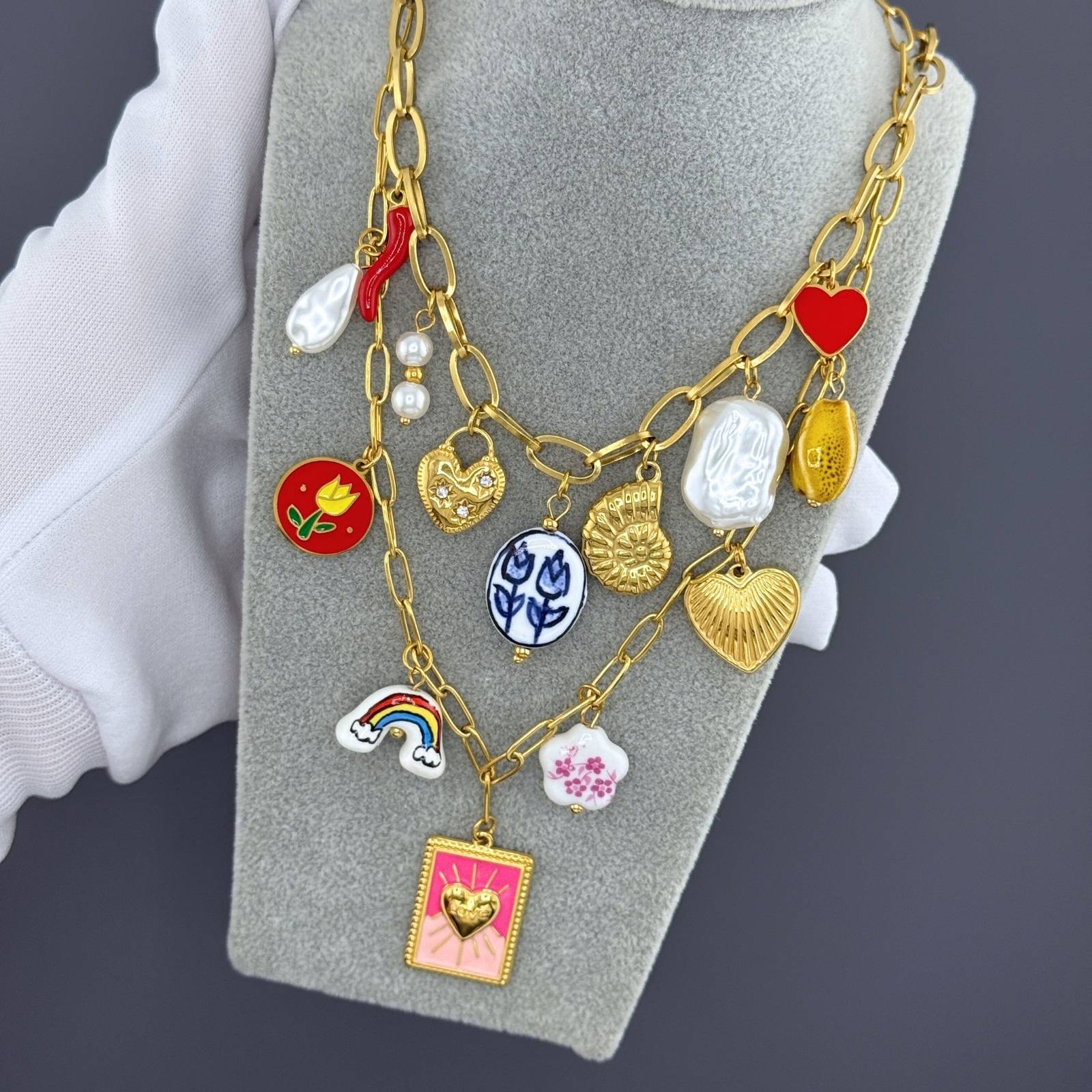 Gold necklace with various charms on a gray stand against a dark background