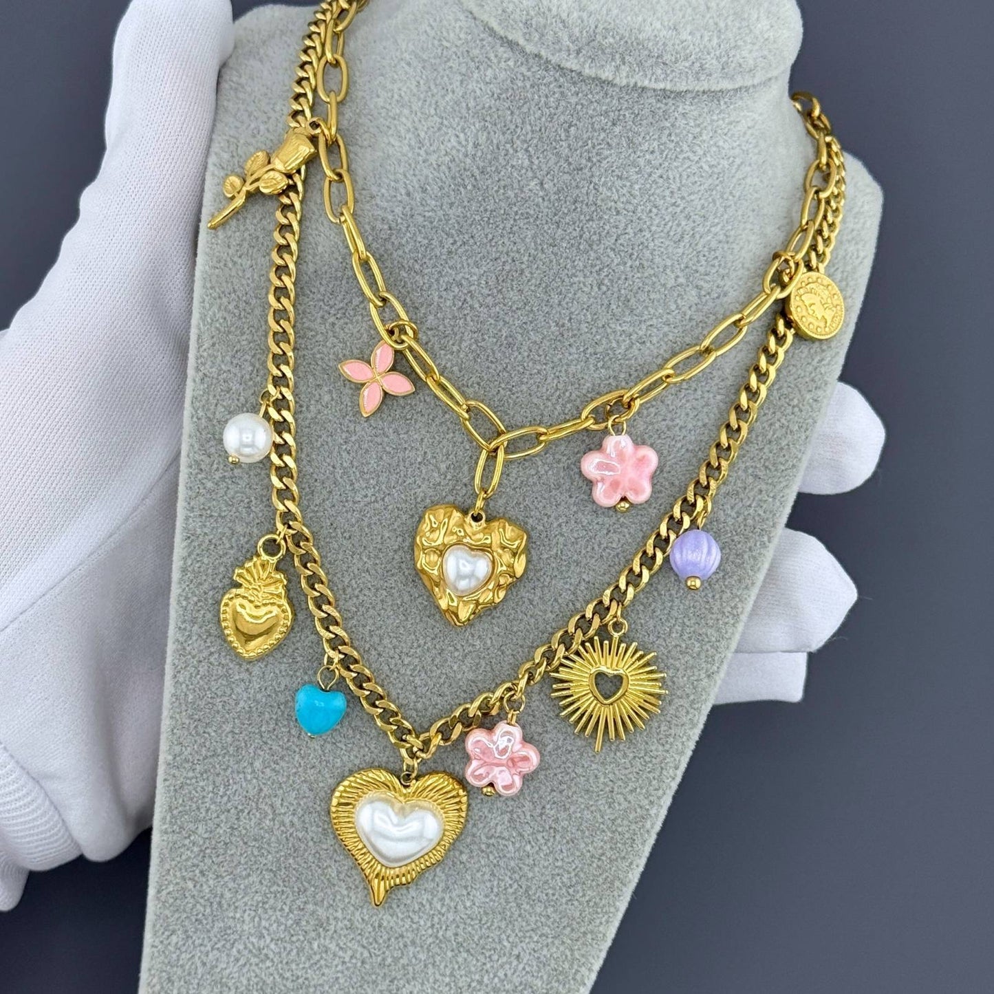 Gold chain necklace with heart and flower charms on a gray stand.