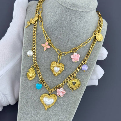 Gold chain necklace with heart and flower charms on a gray stand.
