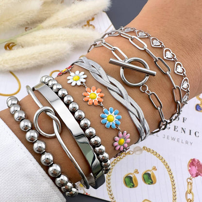 Multiple silver bracelets with various designs on a wrist, with a blurred background.