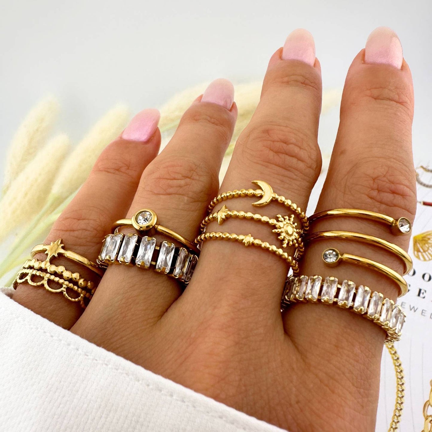 Hand wearing multiple gold rings with various designs on a light background