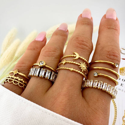 Hand wearing multiple gold rings with various designs on a light background