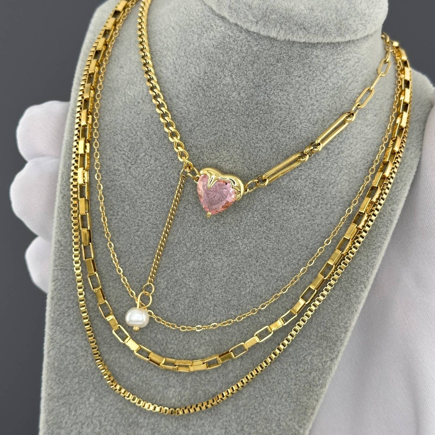 Gold necklaces with a heart-shaped pink pendant and pearl on a grey mannequin bust.