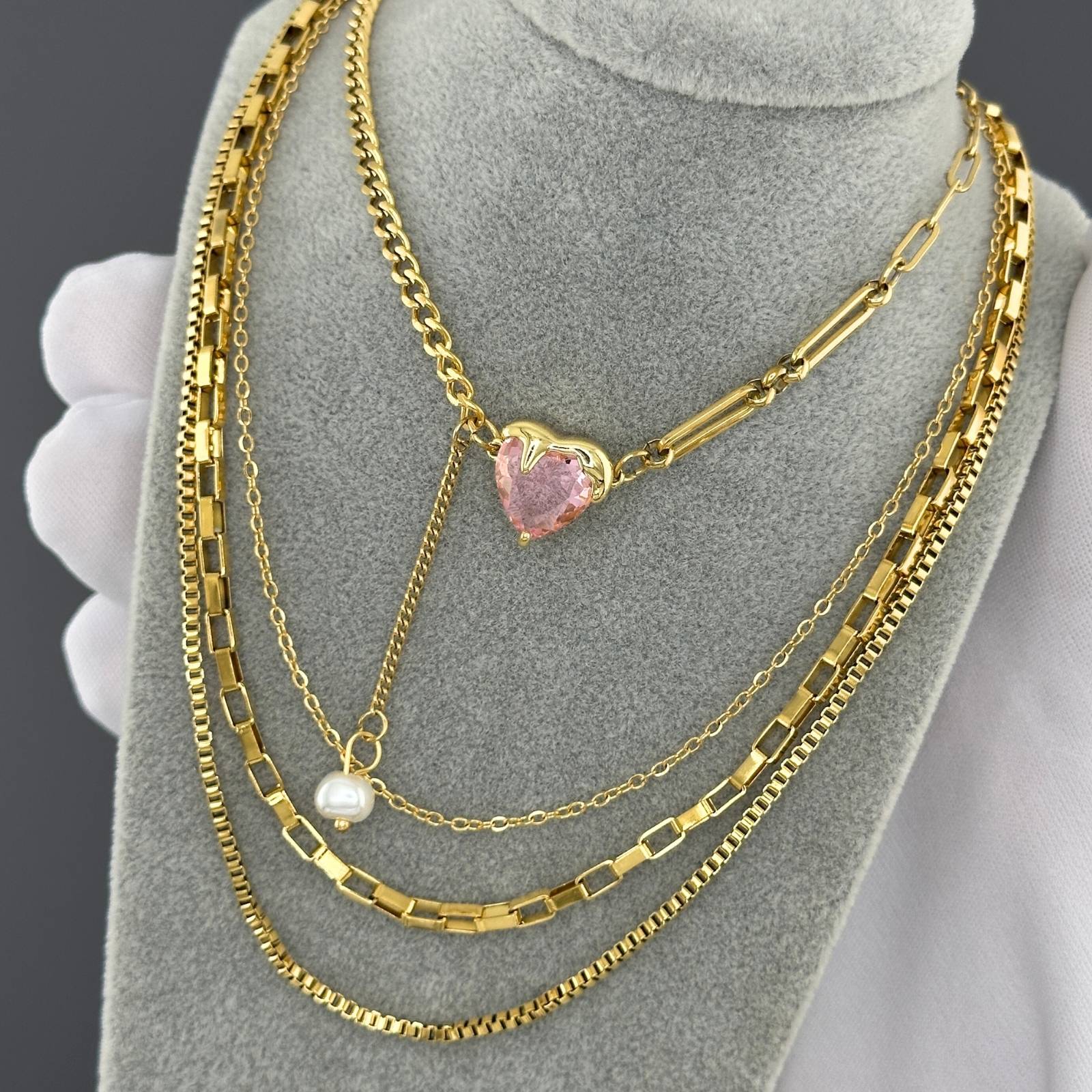 Gold necklaces with a heart-shaped pink pendant and pearl on a grey mannequin bust.