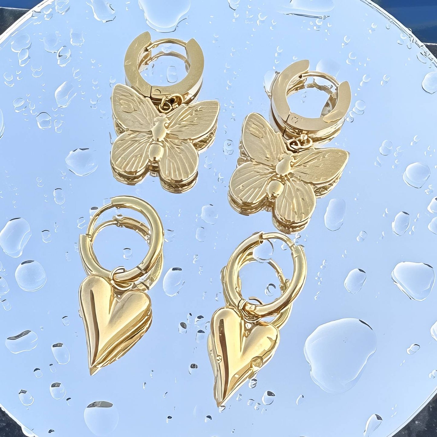 Gold butterfly and heart hoop earrings on a textured blue background