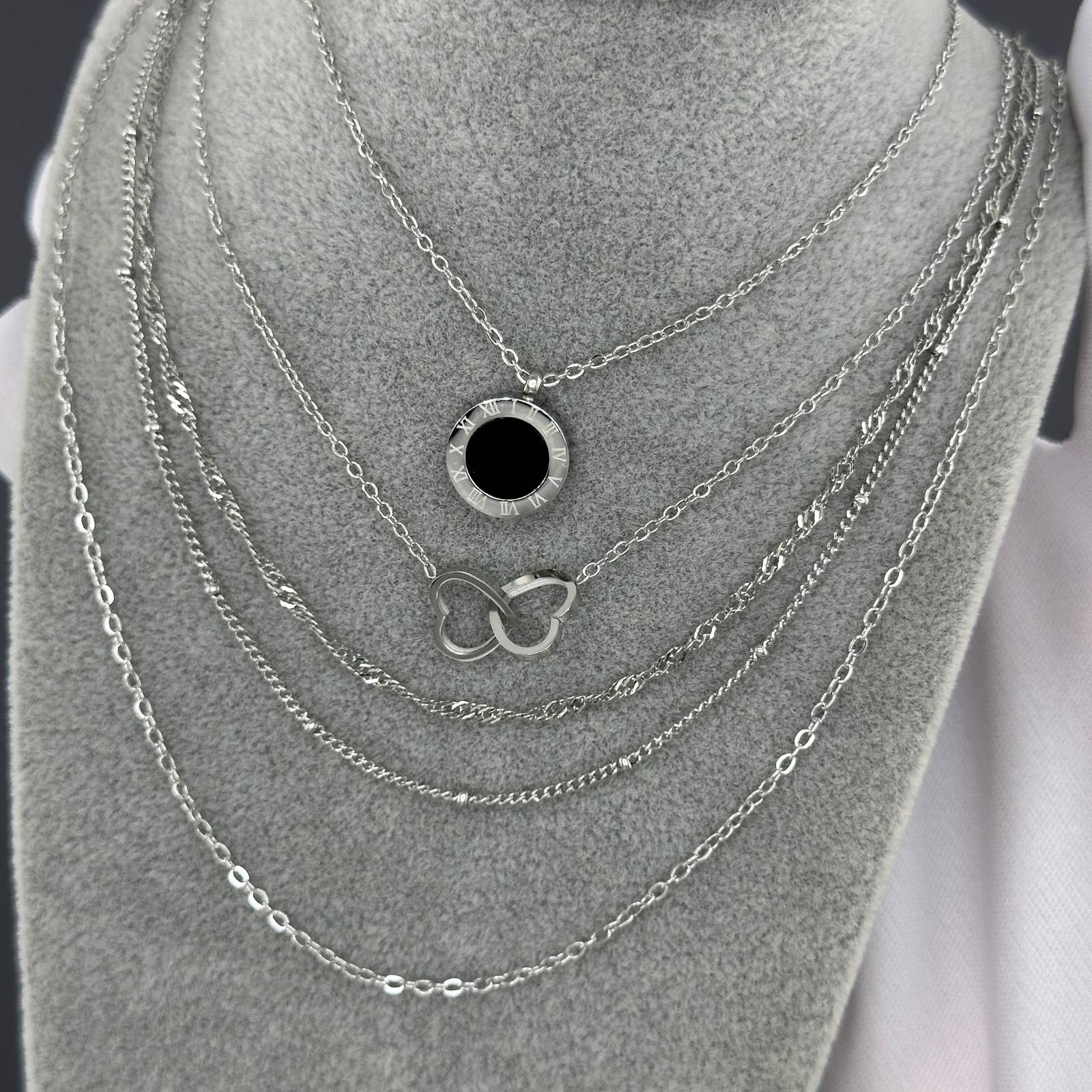 Set of silver necklaces with various pendants on a gray stand.