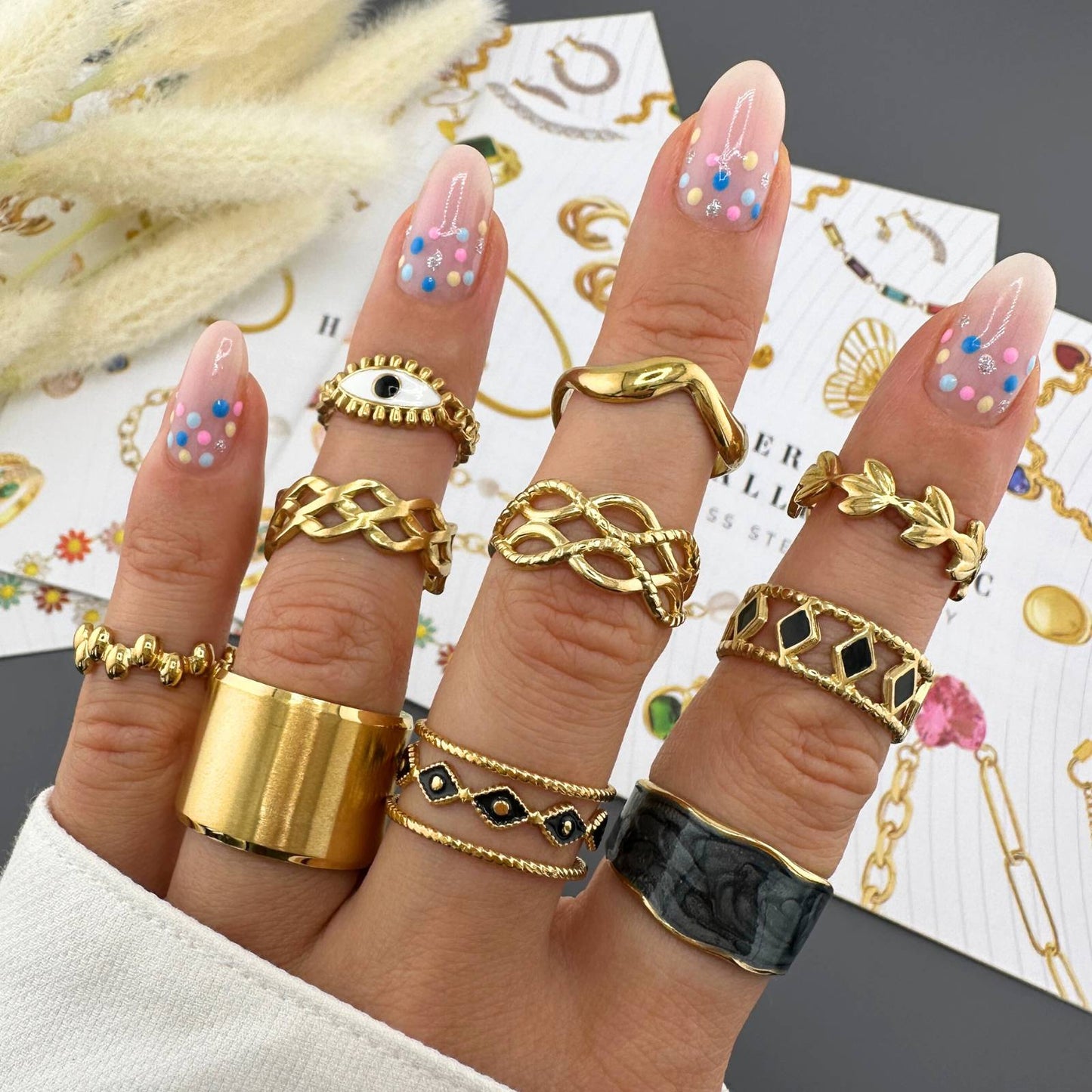 Fingers wearing multiple gold rings with a decorative background