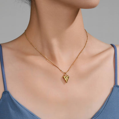 Gold necklace with a heart pendant worn by a person in a blue top against a grey background