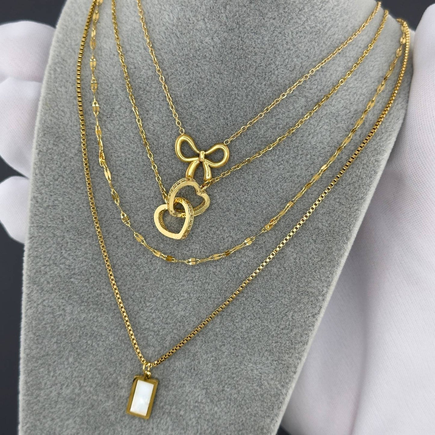 Gold necklaces with heart and bow pendants on a gray stand.
