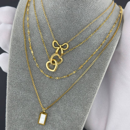 Gold necklaces with heart and bow pendants on a gray stand.