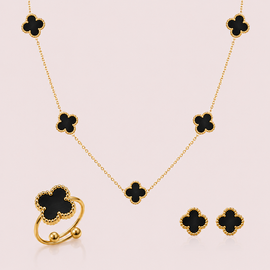 Gold jewelry set with black clover-shaped stones on a light pink background
